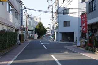 写真５は、駅から来た時の建物前の通りです。正面には石鍋商店があります。